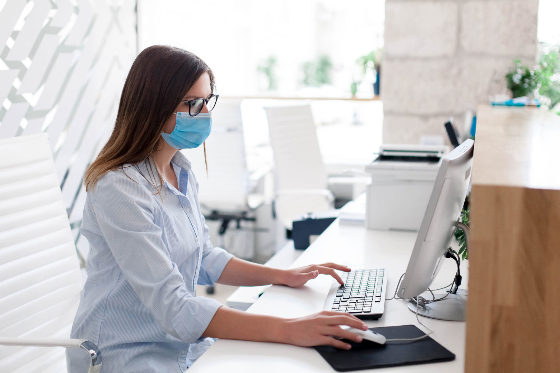 A woman at her desk wearing a face mask, focused on her work in a professional environment.